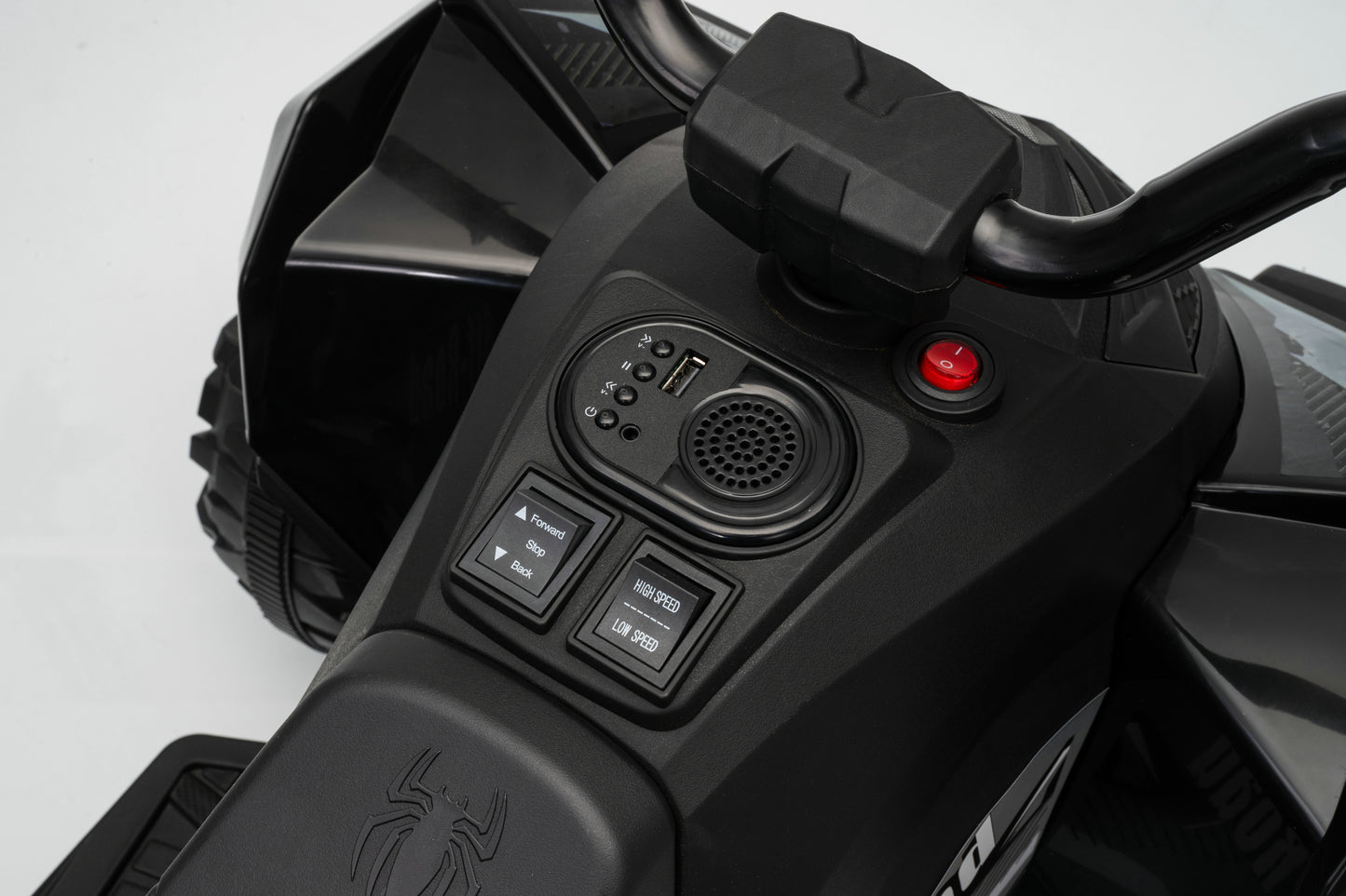 Close-up of a black electric ride-on toy vehicle control panel with buttons, a speaker grille, and a red start button, shown on a white background.
