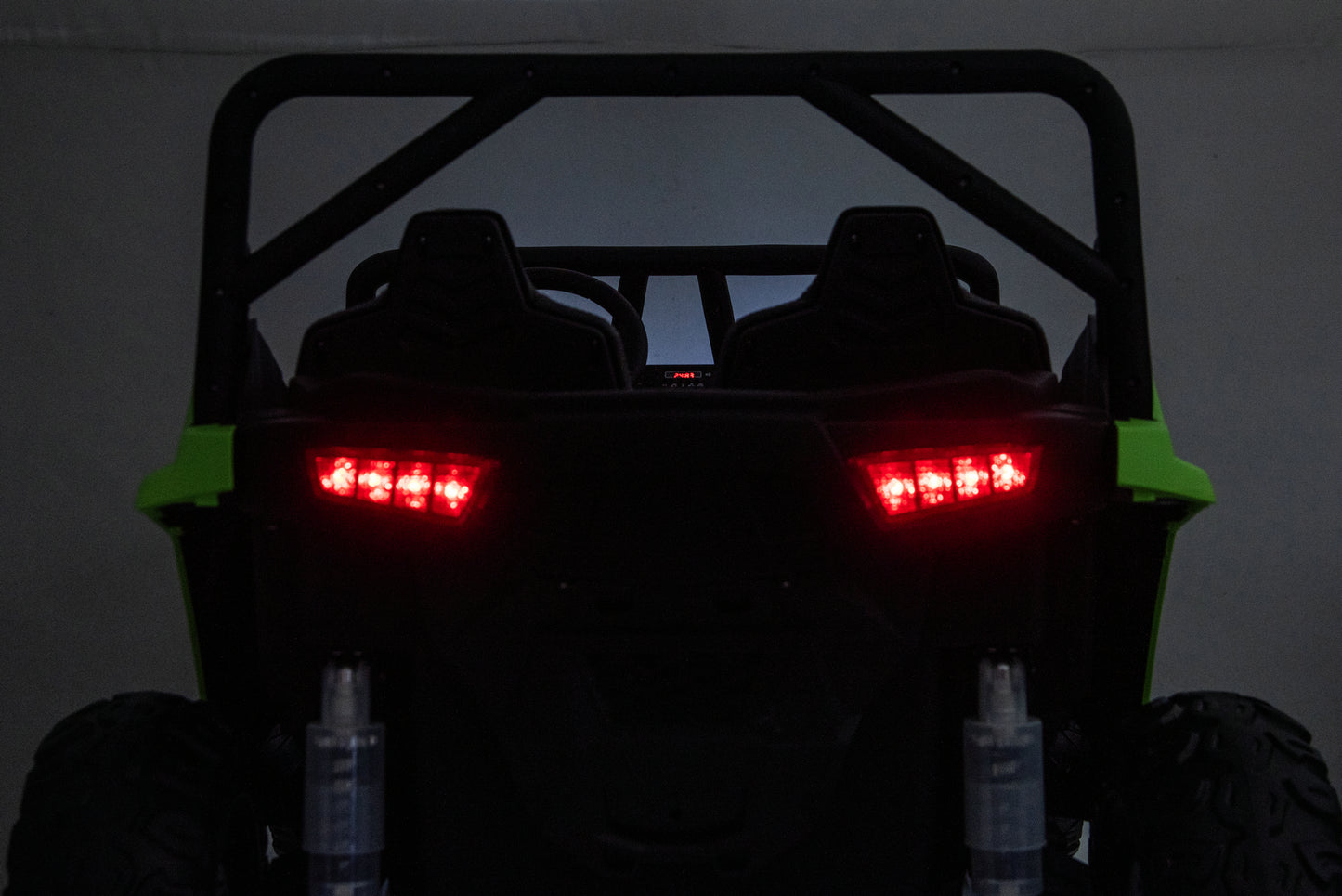 Rear view of a black off-road UTV with bright green side panels and illuminated red LED taillights, photographed in a dark indoor setting.