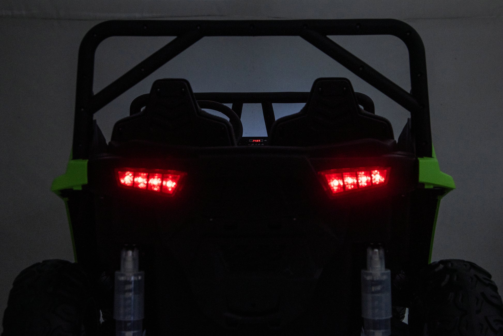 Rear view of a black off-road UTV with bright green side panels and illuminated red LED taillights, photographed in a dark indoor setting.