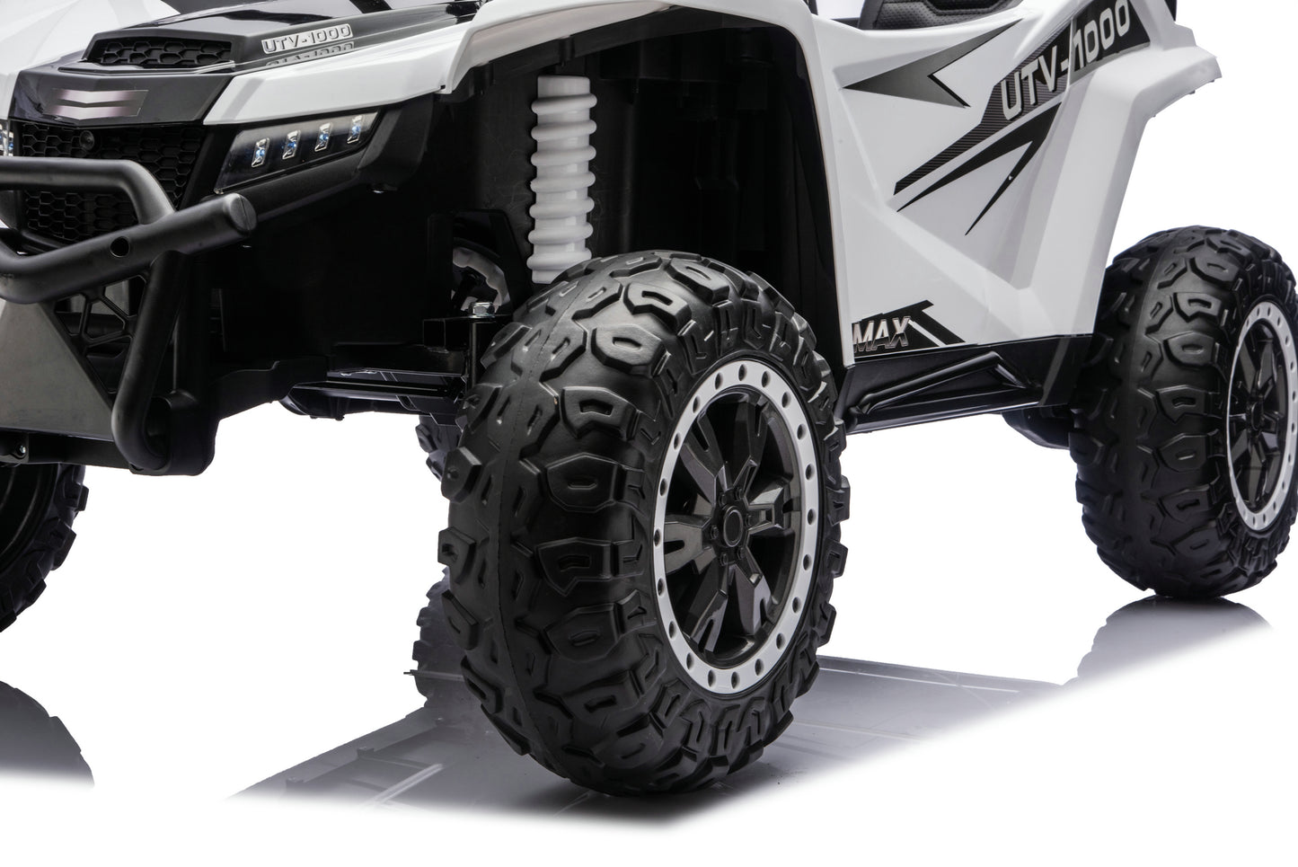 A close-up studio shot of a white and black UTV-style off-road vehicle, showing the front grille, suspension, large black off-road tires, and side body panels with graphic decals.