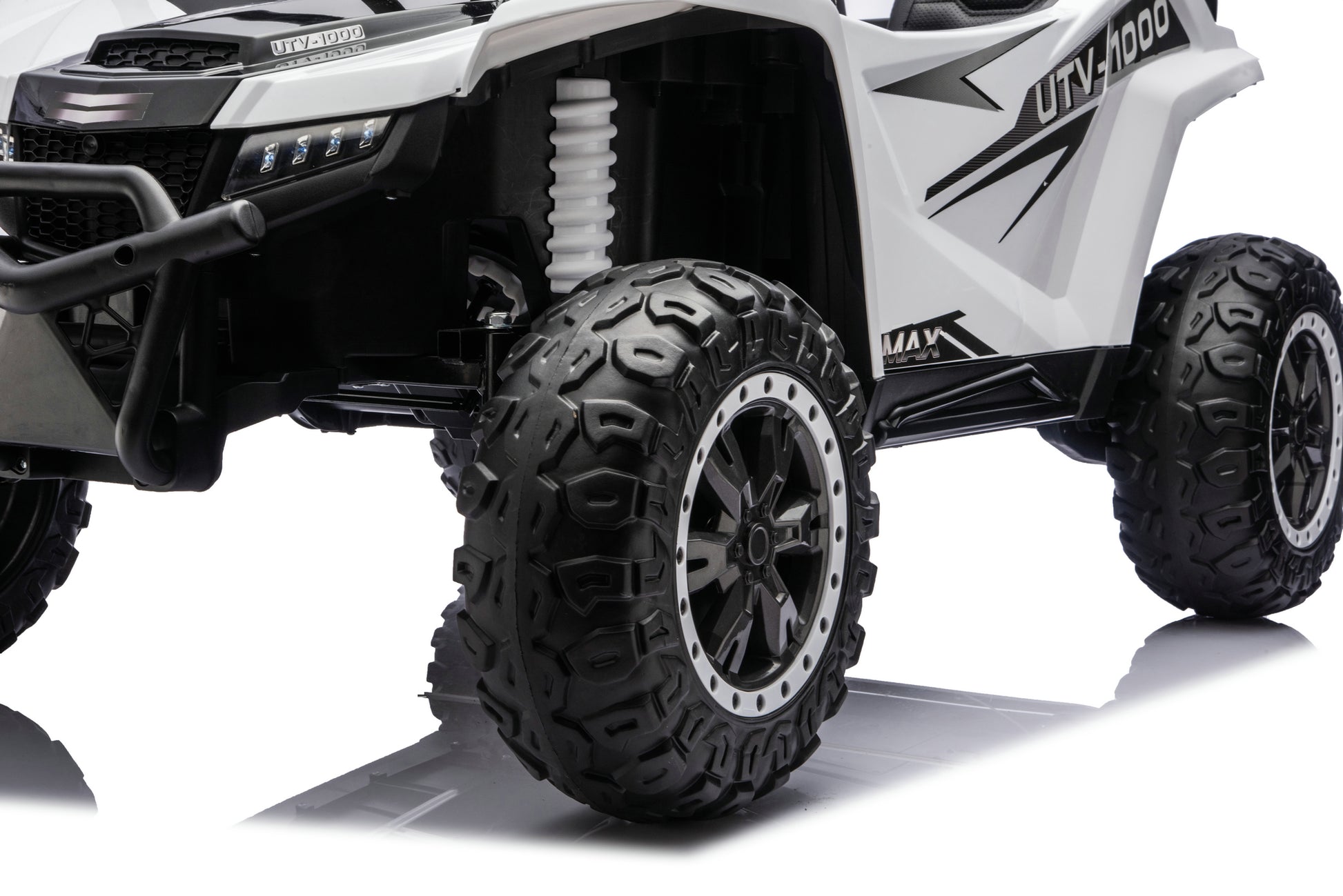 A close-up studio shot of a white and black UTV-style off-road vehicle, showing the front grille, suspension, large black off-road tires, and side body panels with graphic decals.