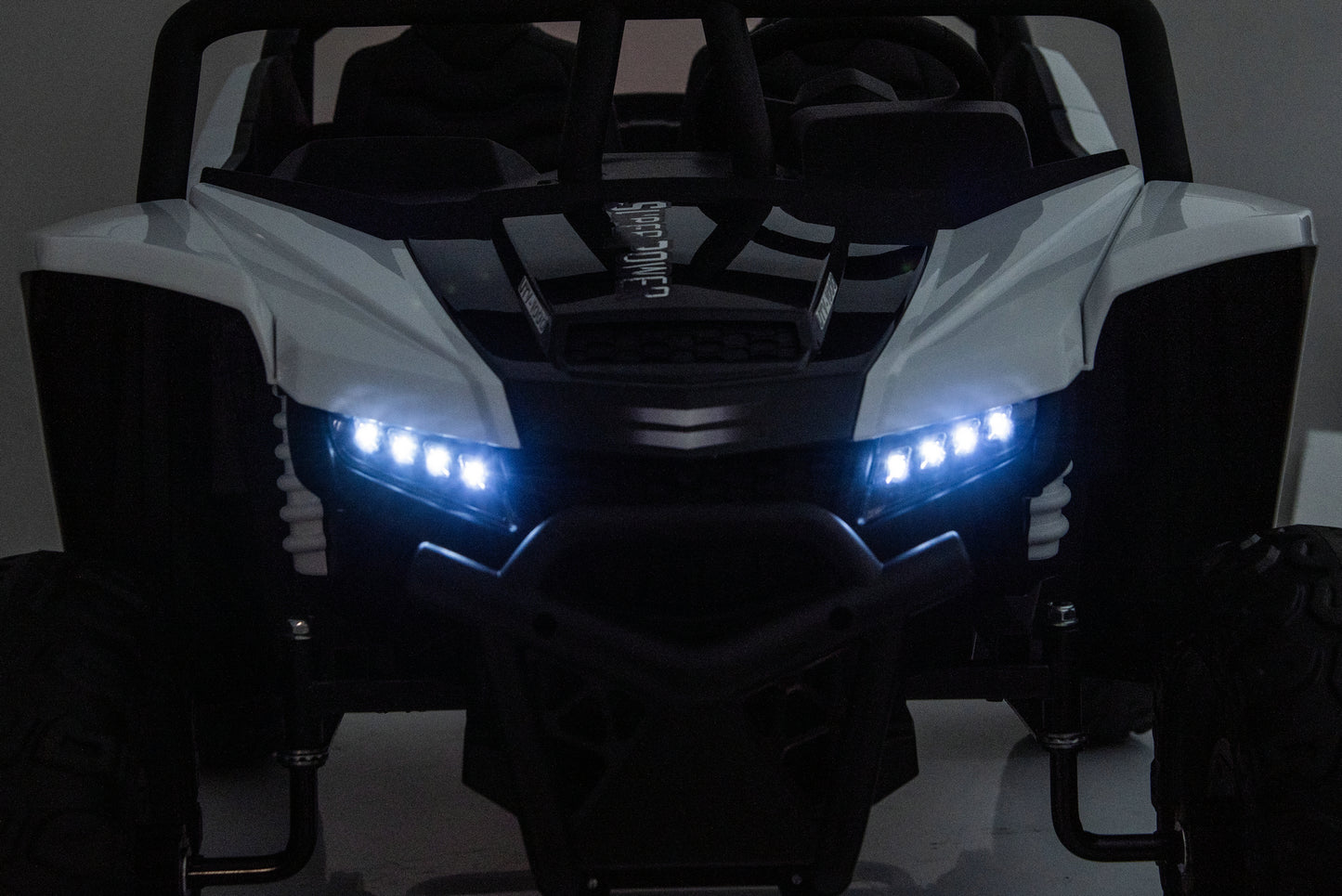 A white and black off-road vehicle or UTV shown from the front in a dark setting, with bright blue LED headlights turned on.