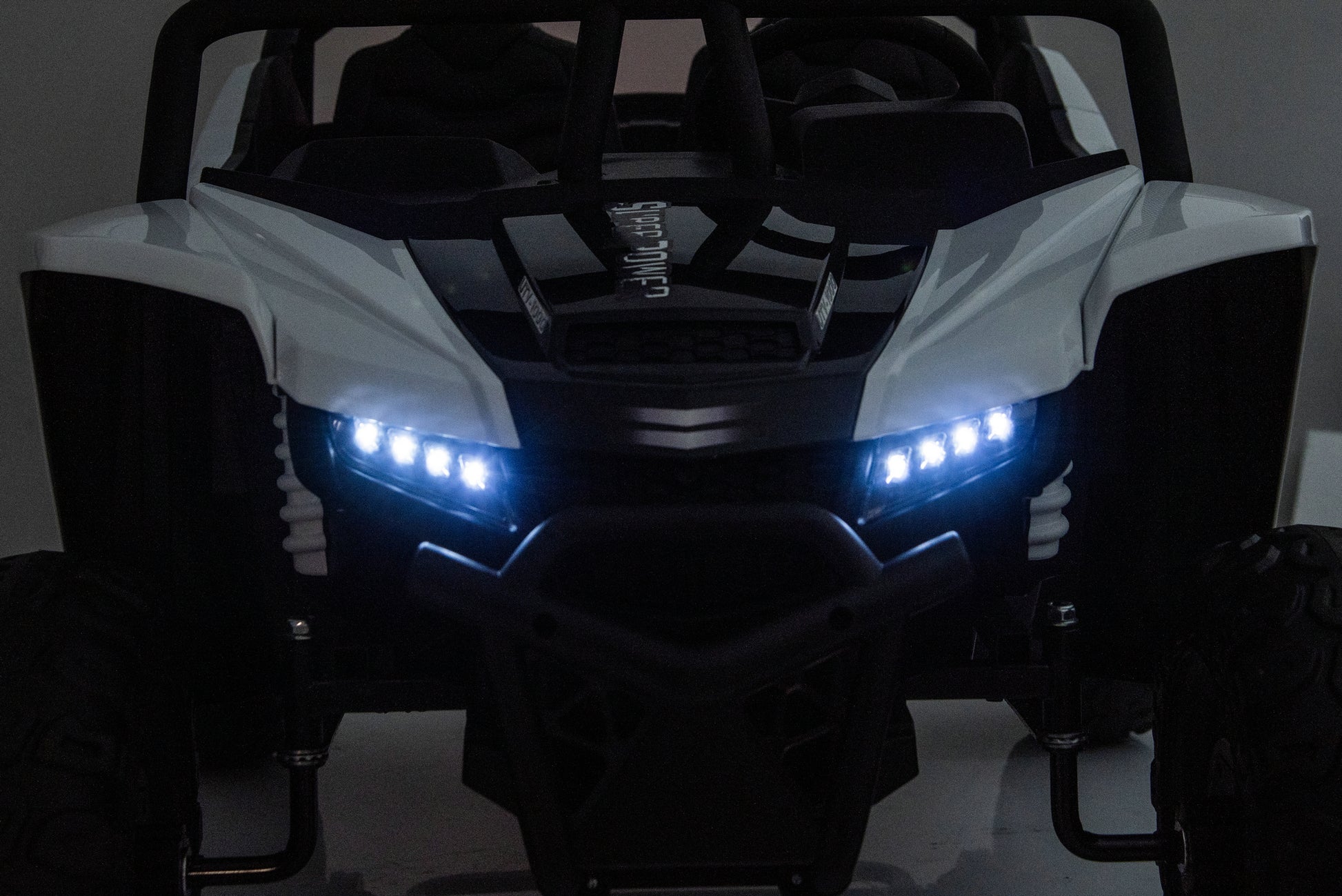 A white and black off-road vehicle or UTV shown from the front in a dark setting, with bright blue LED headlights turned on.