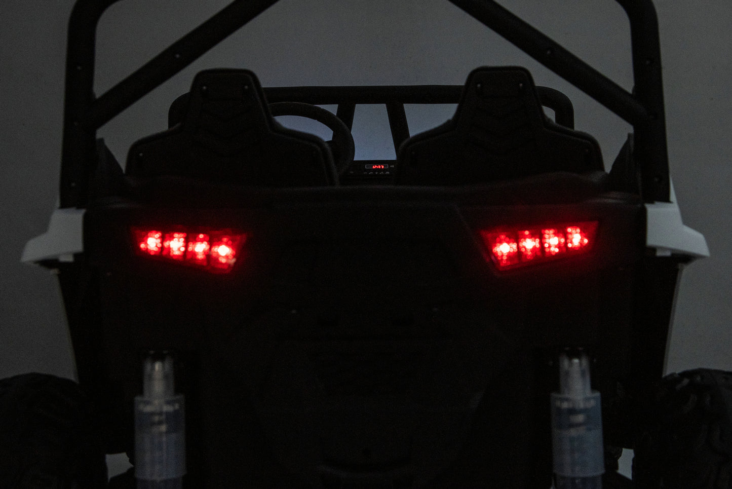 Rear view of a black off-road vehicle or UTV with illuminated red LED taillights, shown against a dark gray background.