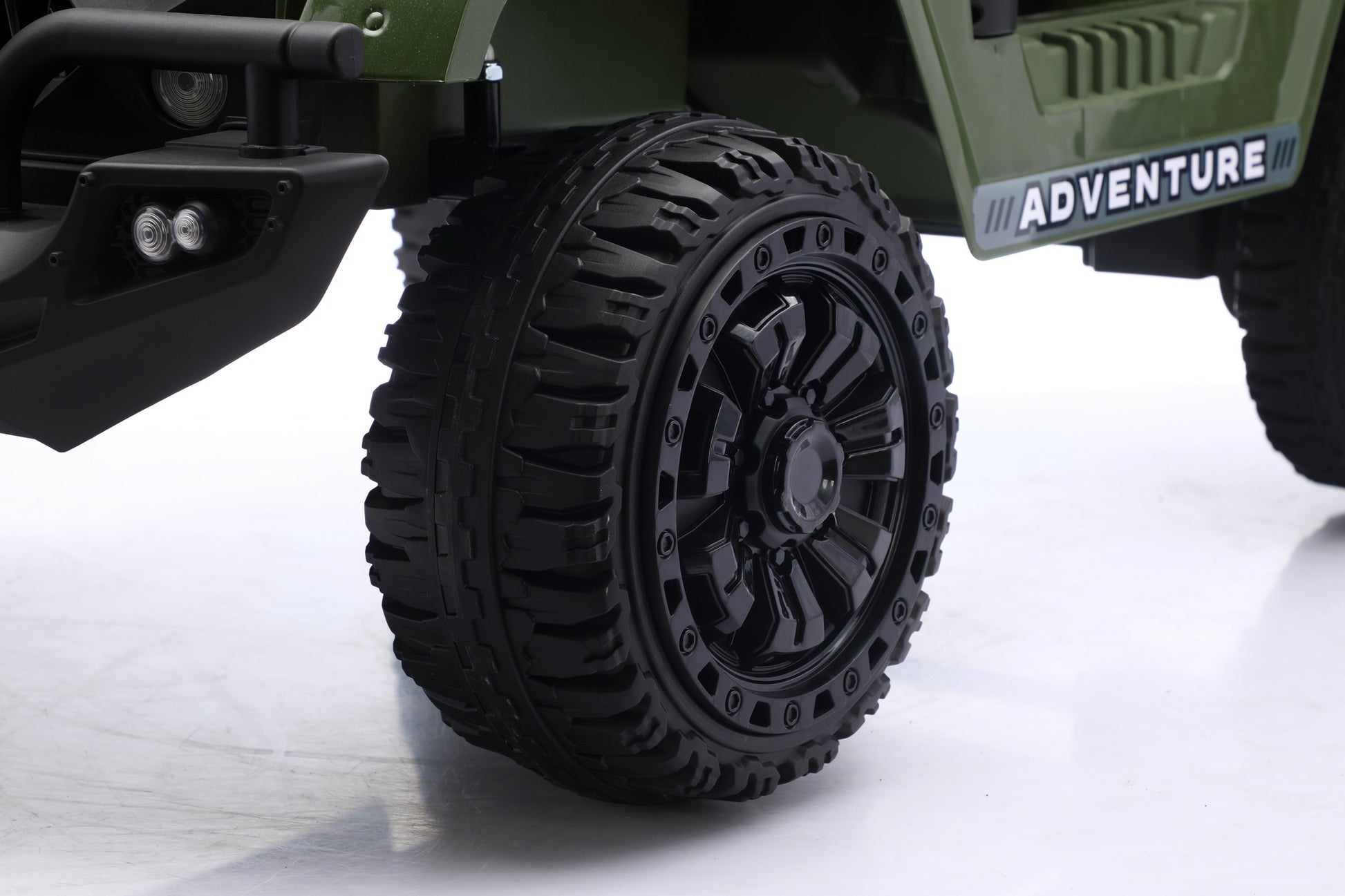 Close-up of a black off-road tire and black multi-spoke wheel on an olive green vehicle with 'ADVENTURE' written on the side panel.